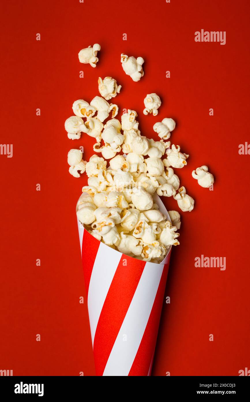 Composizione piatta con popcorn in un cono di carta su sfondo rosso. Foto Stock