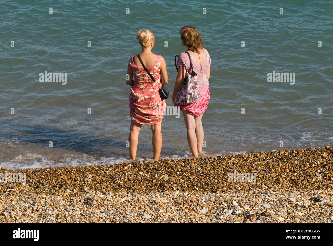 Le donne amiche Eastbourne Beach 2 donne che chiacchierano, si sono tolte le scarpe e si trovano in riva al mare. Hanno indossato i loro abiti estivi per evitare che si bagnino. Eastbourne, East Sussex, Inghilterra 28 agosto 2013. 2010 UK HOMER SYKES Foto Stock