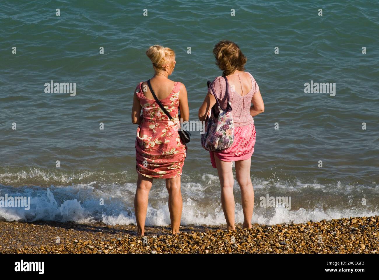 Due donne hanno indossato i loro abiti estivi per evitare che si bagnino. Eastbourne Beach 2 donne amiche che chiacchierano, si sono tolte le scarpe e sono in piedi sul bordo dell'acqua. Eastbourne, East Sussex, Inghilterra 28 agosto 2013. 2010 UK HOMER SYKES Foto Stock