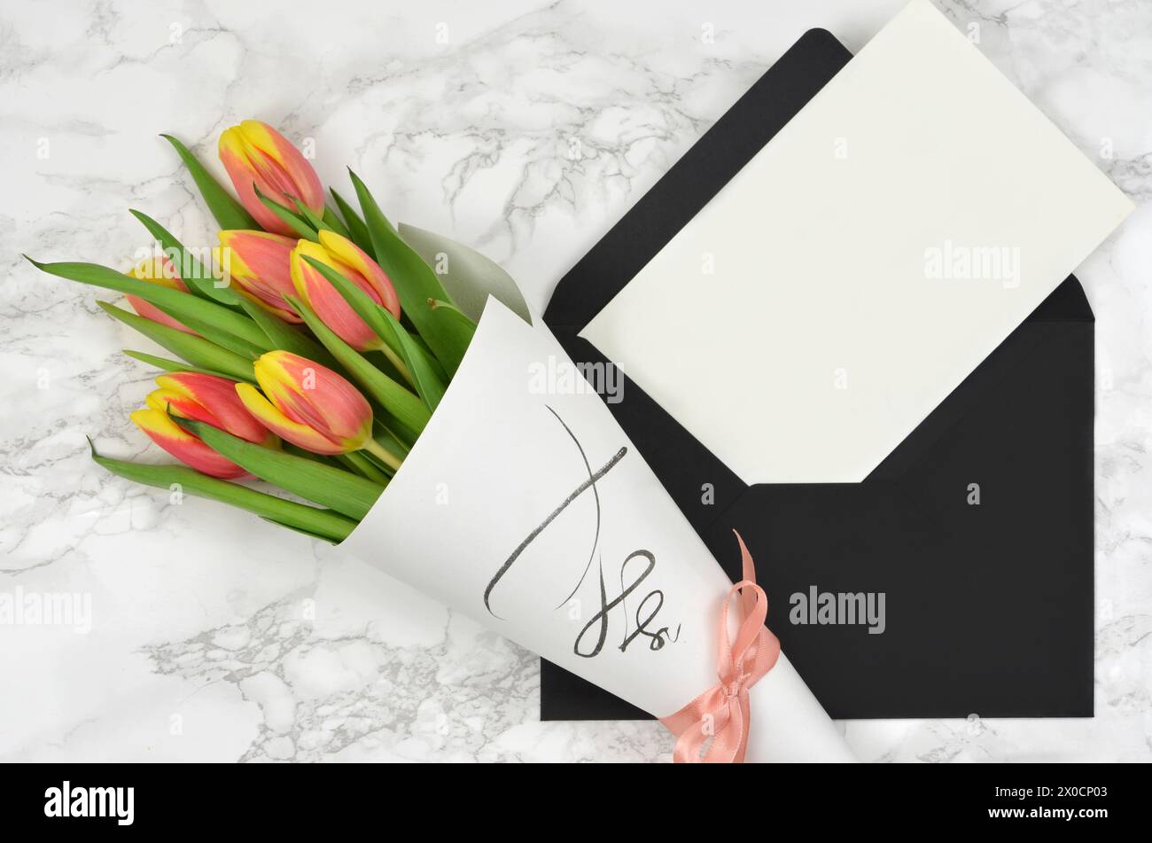 Bouquet di tulipani e foglio di carta bianco con molto spazio per riempire il contenuto, busta nera. Vista dall'alto. Foto Stock
