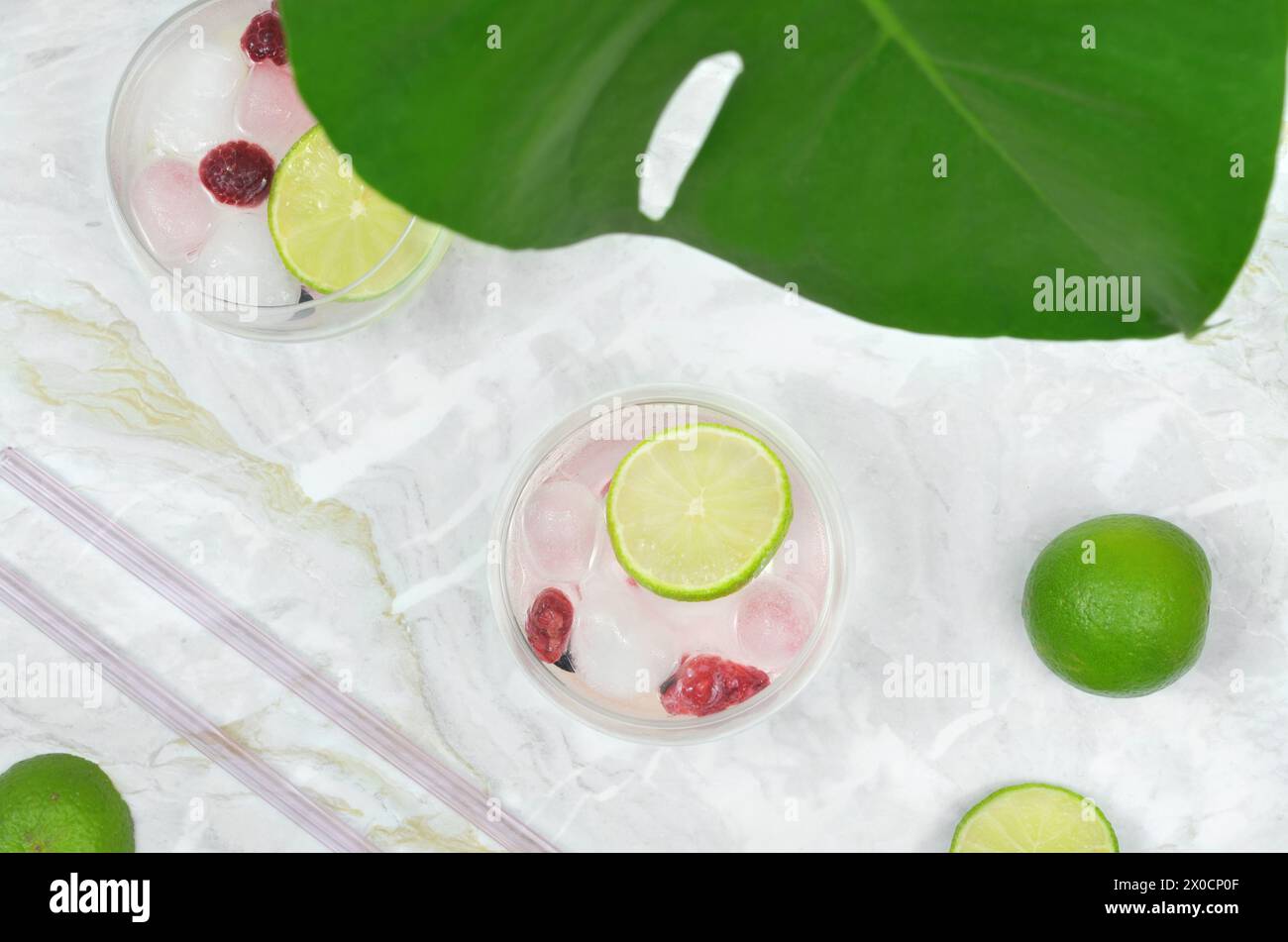 Drink con vista dall'alto decorati con fette di lime e lamponi. Foglia di Monstera. Foto Stock