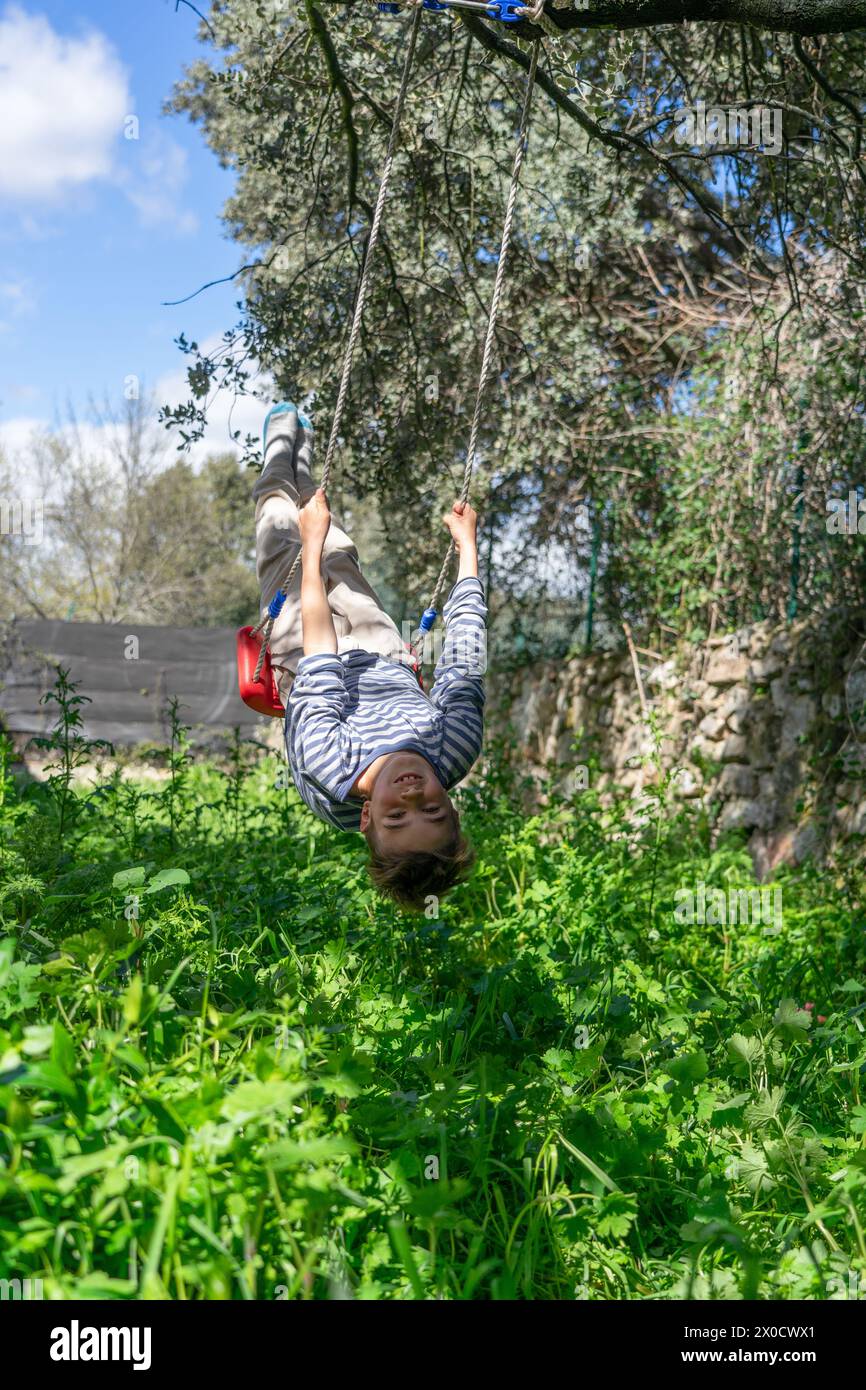 Bambino caucasico di 8 anni che oscilla su un'altalena appesa ad un albero in natura Foto Stock