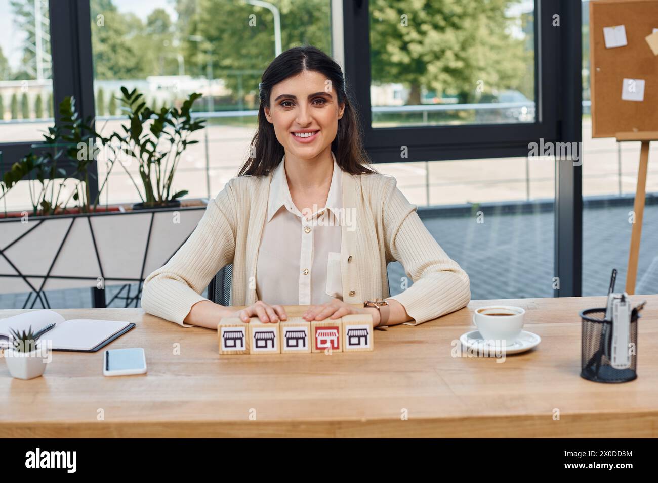 Una donna d'affari seduta a un tavolo, circondata da blocchi, a riflettere sulla sua prossima mossa nel mondo delle franchigie. Foto Stock