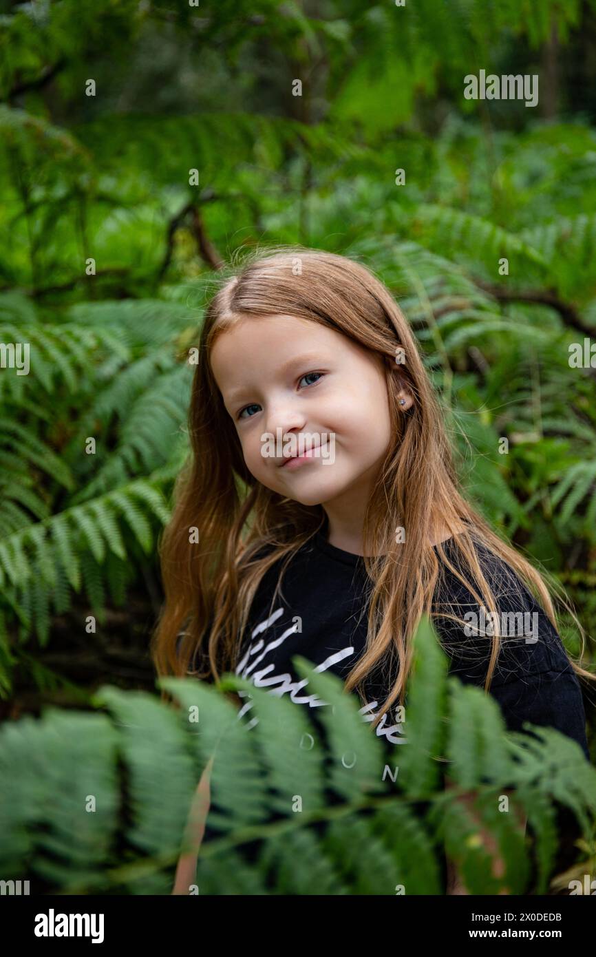 Sorridente ragazza bruna lunga e bruna in una foresta di felci verde nascosta nella natura Foto Stock