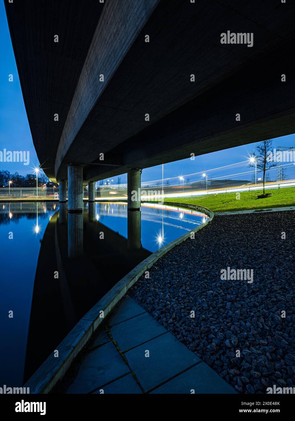 Una scena tranquilla si dispiega mentre il crepuscolo cade su Goteborg, Svezia, guardando da sotto un ponte mentre si estende sull'acqua ferma. L'architettura dei ponti c Foto Stock