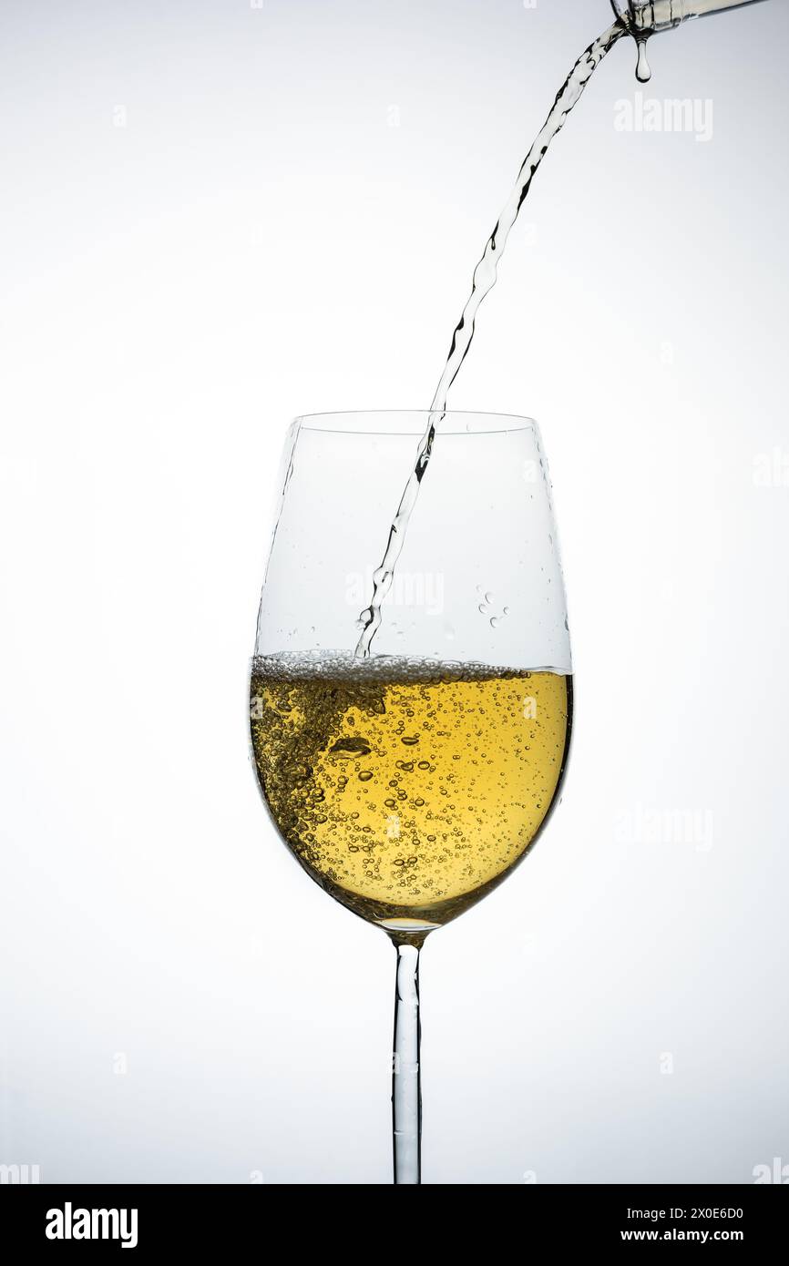 bicchiere di vino bianco con bottiglia che versa il liquido su uno sfondo chiaro Foto Stock