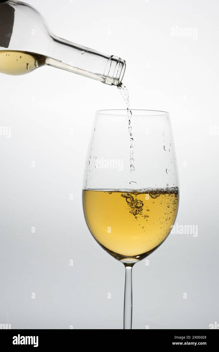 bicchiere di vino bianco con bottiglia che versa il liquido su uno sfondo chiaro Foto Stock