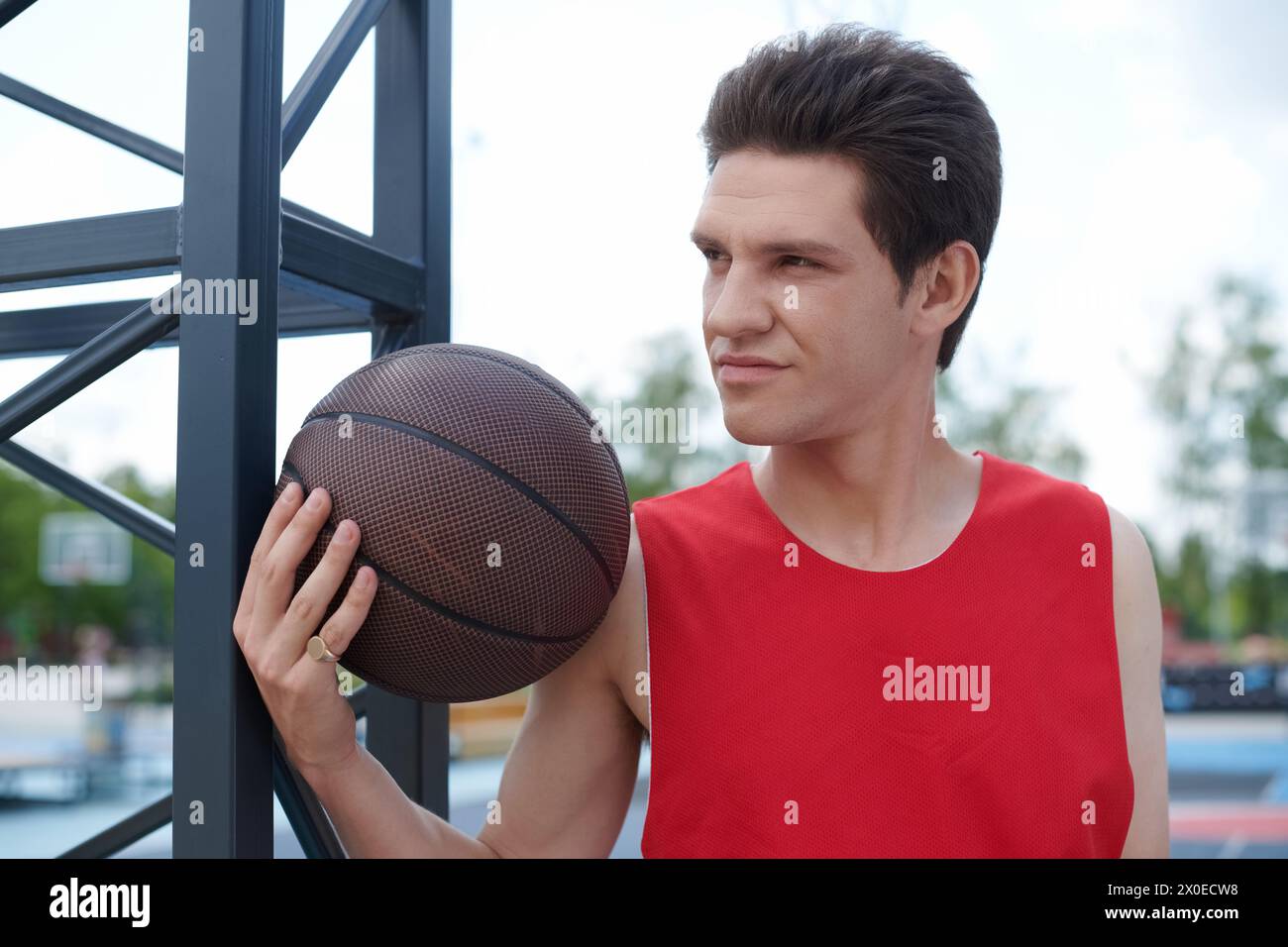 Un uomo con una camicia rossa infuocata dona abilmente un pallacanestro all'aperto in una giornata estiva di sole. Foto Stock