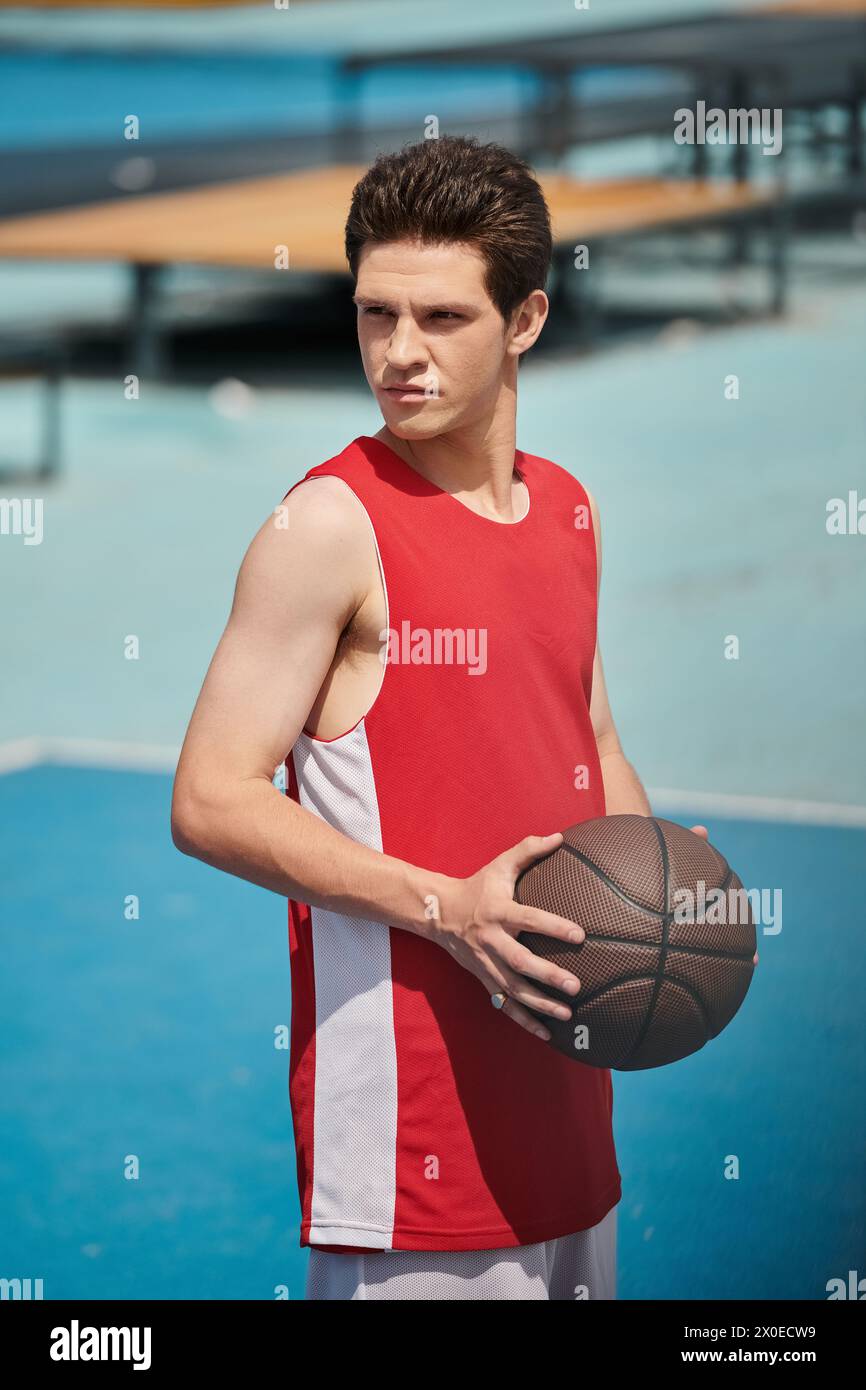 Un giovane giocatore di basket su un campo che tiene abilmente la palla in una giornata estiva di sole. Foto Stock