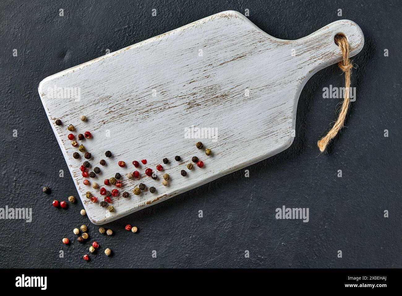 Tagliere di legno bianco e grani di pepe multicolore su un tavolo di cemento nero Foto Stock
