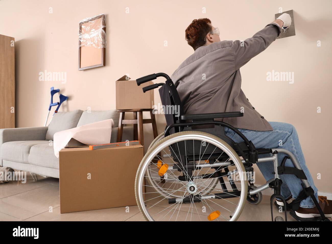 Giovane uomo in sedia a rotelle che si arrampica sul muro durante la riparazione a casa Foto Stock