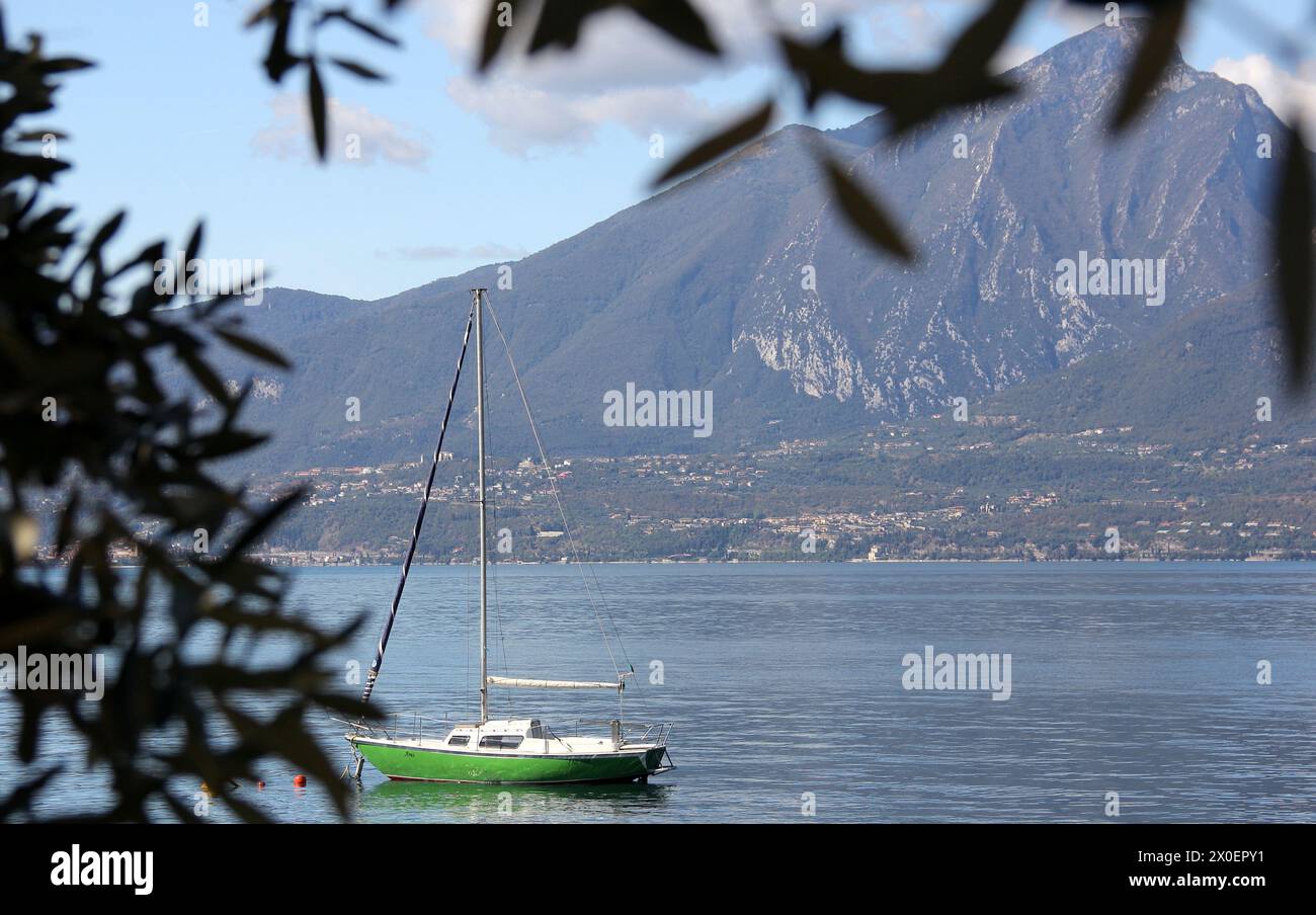 Barca a vela verde sul Lago di Garda vicino a Torri del Benaco, Monte Pizzocolo attraverso il lago sullo sfondo, Italia Foto Stock