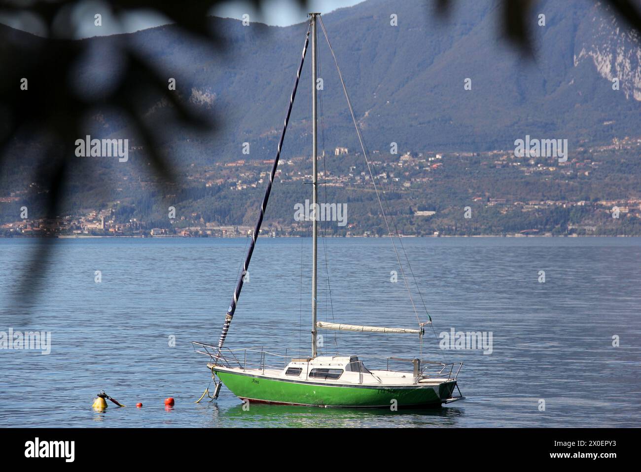 Barca a vela verde sul Lago di Garda vicino a Torri del Benaco, Monte Pizzocolo attraverso il lago sullo sfondo, Italia Foto Stock