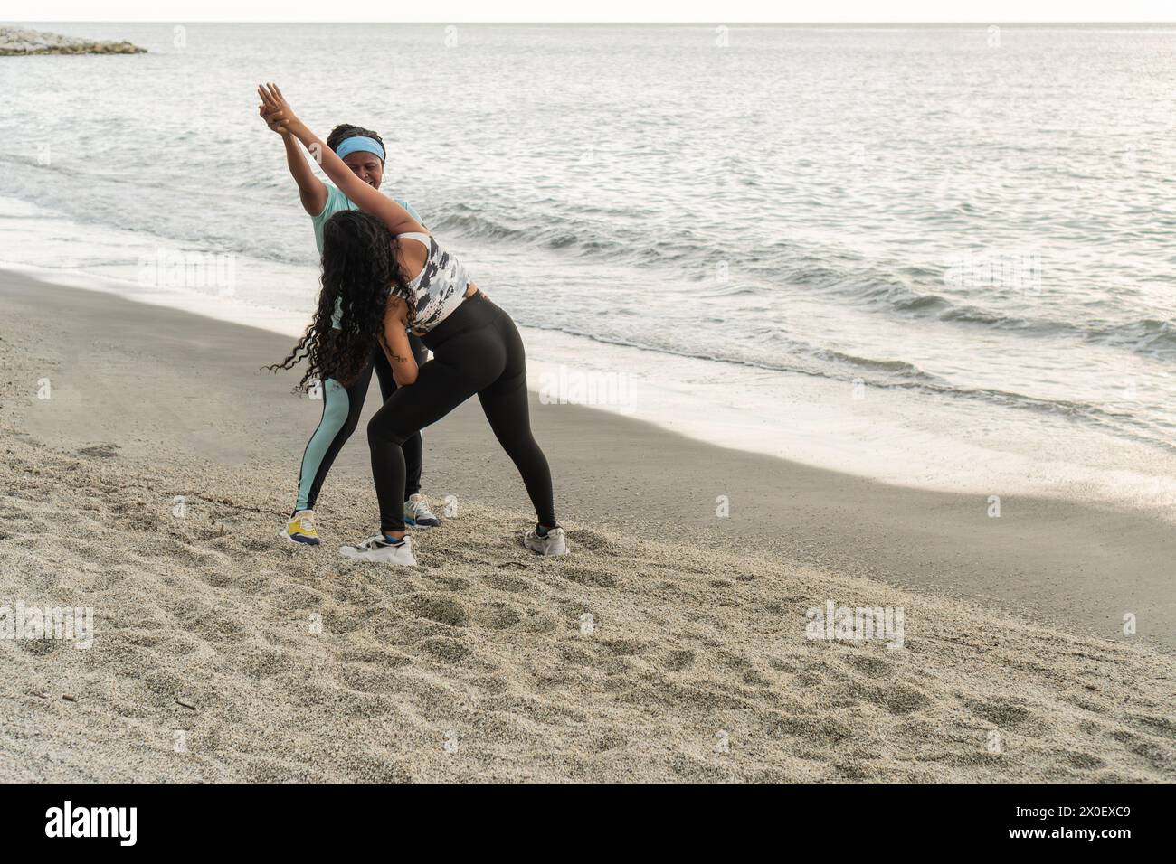 Due donne atletiche impegnate in esercizi di stretching su una spiaggia tranquilla. Foto Stock