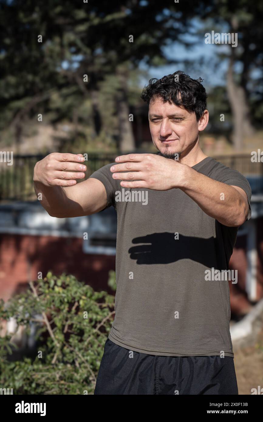 Un uomo caucasico di mezza età adotta la postura statica dell'abbraccio degli alberi, una tecnica cruciale nella pratica chi Kung. Foto Stock