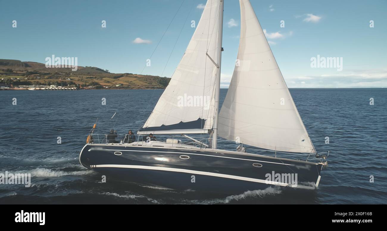 Riflesso del sole sullo yacht di lusso da vicino sull'antenna della baia dell'oceano. Vele bianche a vento sulla barca passeggeri. Regata in mare aperto. Tranquillo e tranquillo paesaggio marino del Golfo di Brodick, dell'isola di Arran, della Scozia, dell'Europa Foto Stock