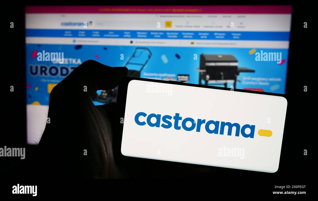 Persona che detiene un telefono cellulare con il logo della catena di negozi di articoli per il miglioramento della casa Castorama davanti alla pagina Web aziendale. Mettere a fuoco il display del telefono. Foto Stock