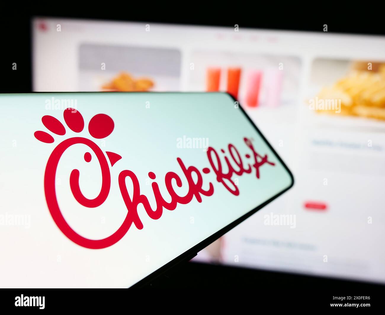 Smartphone con logo della società americana di fast food Chick-fil-A Inc. Davanti al sito Web aziendale. Mettere a fuoco la parte sinistra del display del telefono. Foto Stock