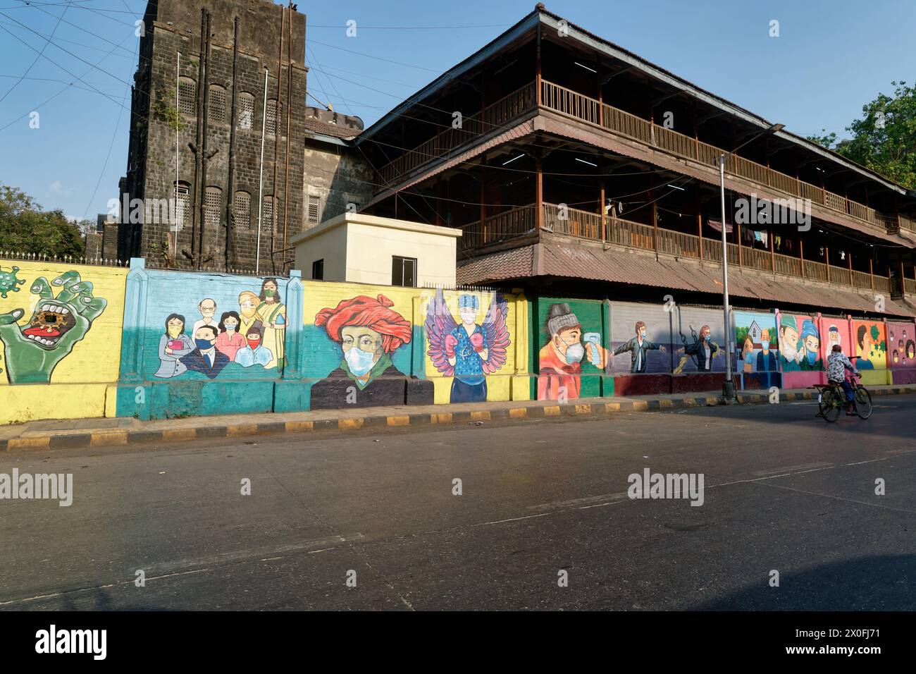 Una lunga parete a Mumbai, India, situata di fronte ad un edificio storico e decorata con colorati murales a tema Covid-19 Foto Stock