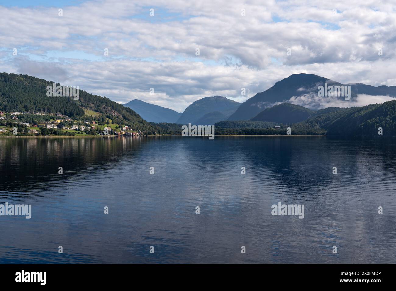 Le calme acque di Stangvikfjorden rispecchiano il cielo, con il villaggio di Kvanne annidato contro le montagne. Destinazione di viaggio scandinava in estate Foto Stock