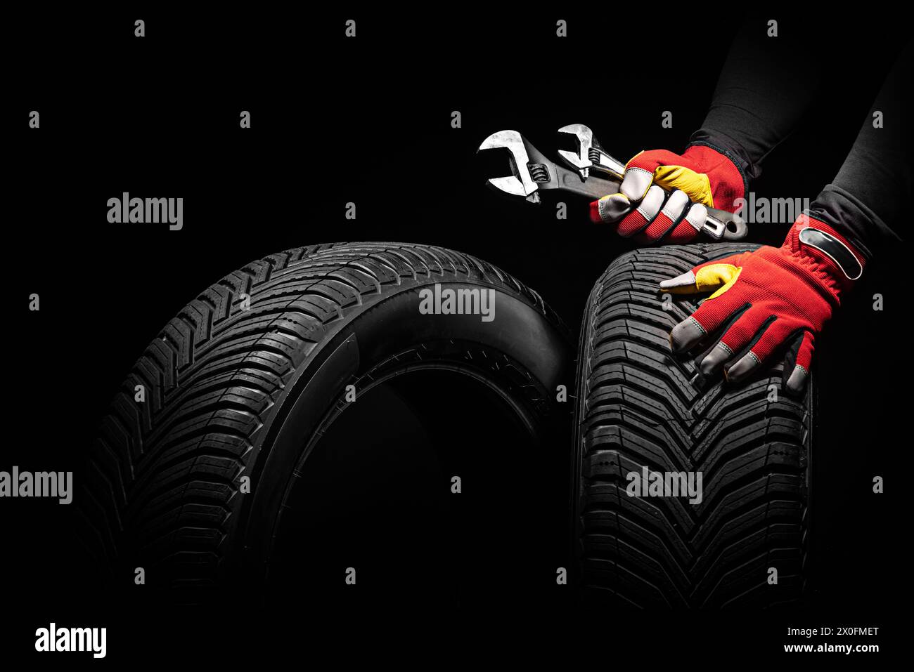 Assistenza pneumatici per auto e mani del meccanico che reggono pneumatico e chiave nuovi su sfondo nero con spazio per testo Foto Stock