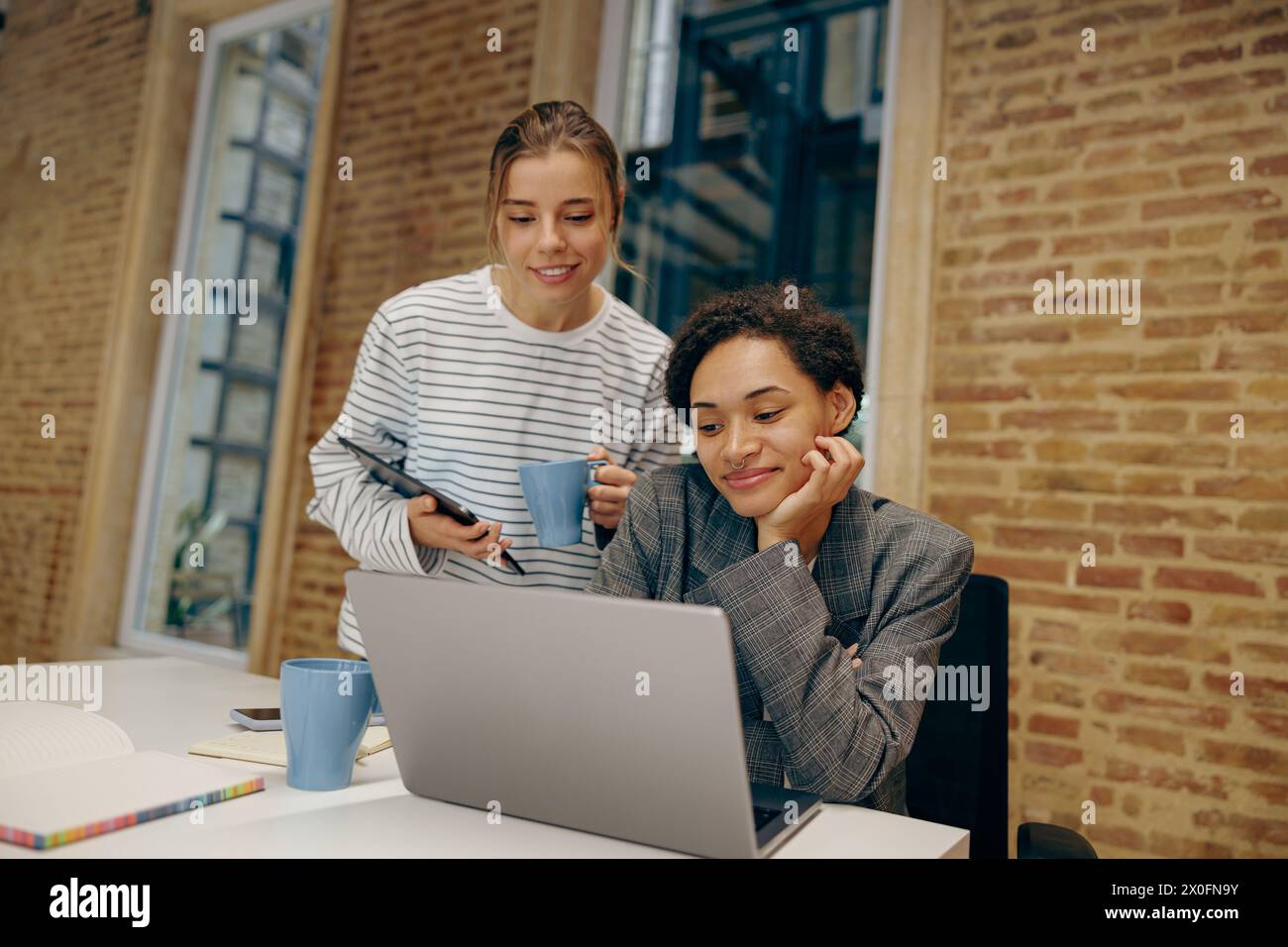 Due colleghi donne concentrate che lavorano insieme al progetto e utilizzano un laptop seduto in ufficio Foto Stock
