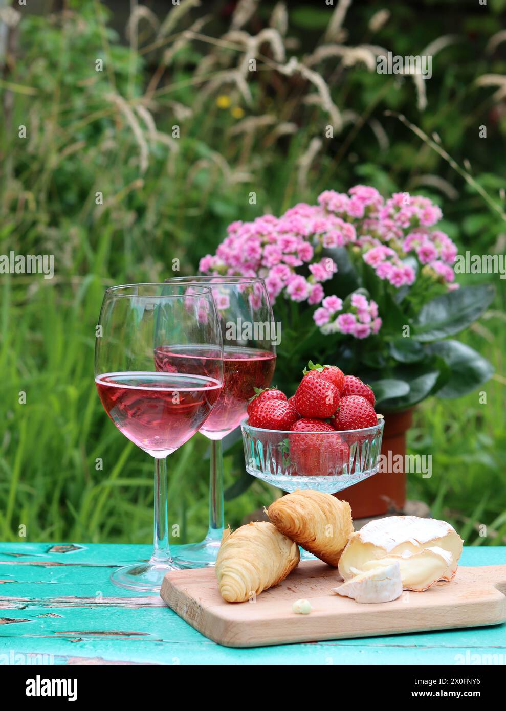 Colazione romantica in giardino. Fine settimana del giorno d'estate. Due bicchieri di spumante, croissant, fragole, formaggio e fiori rosa su un tavolo. Foto Stock