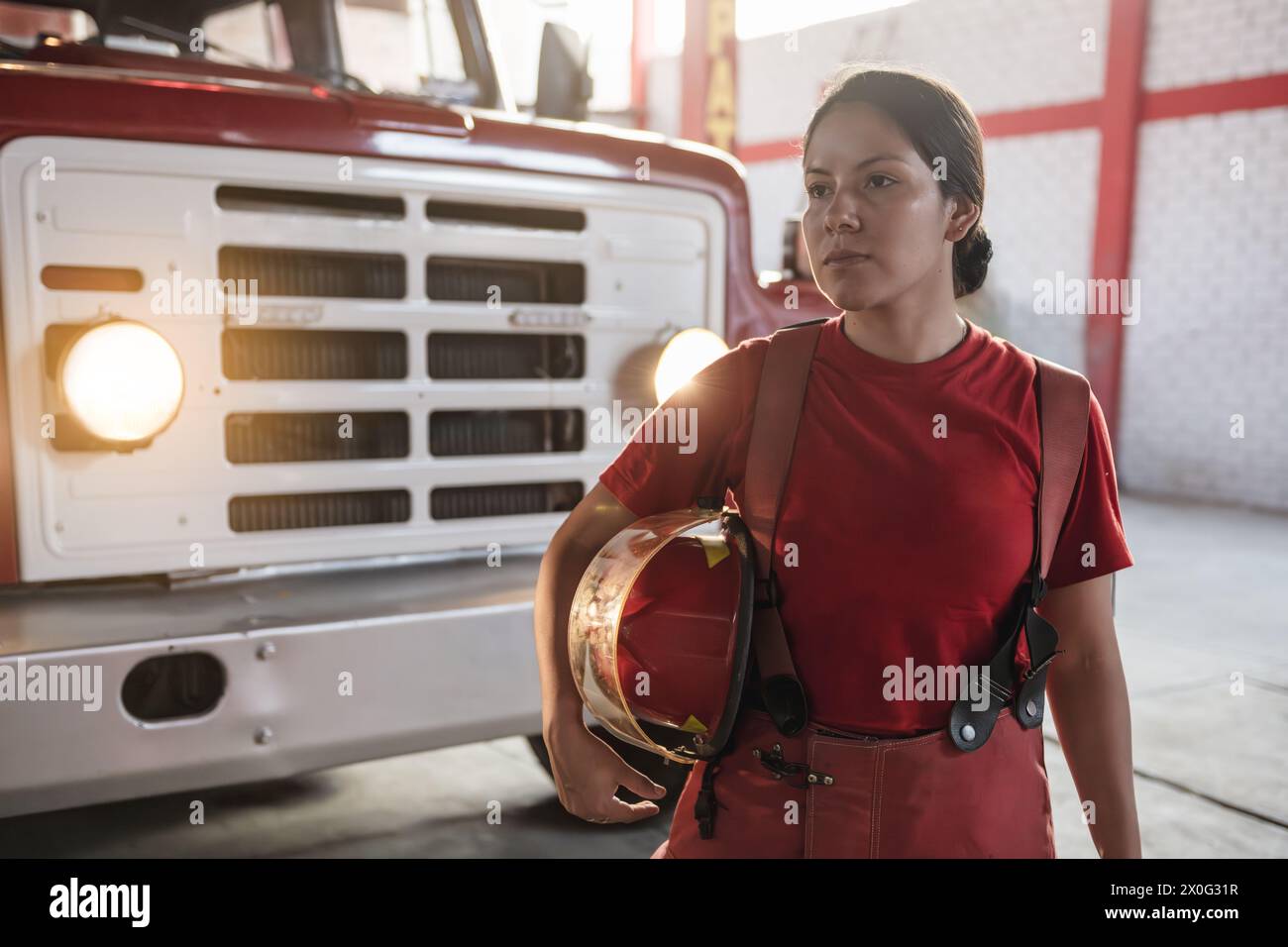 Ritratto di donna vigile del fuoco che guarda in lontananza davanti alla stazione dei pompieri Foto Stock