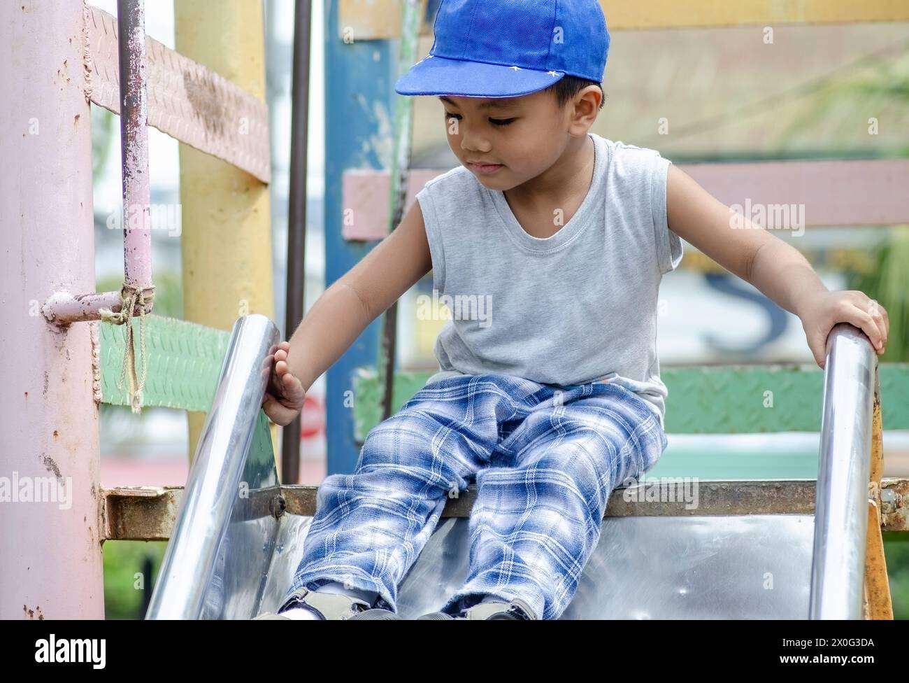 Il ragazzo della scuola materna sta per scivolare giù per lo scivolo nel parco giochi Foto Stock