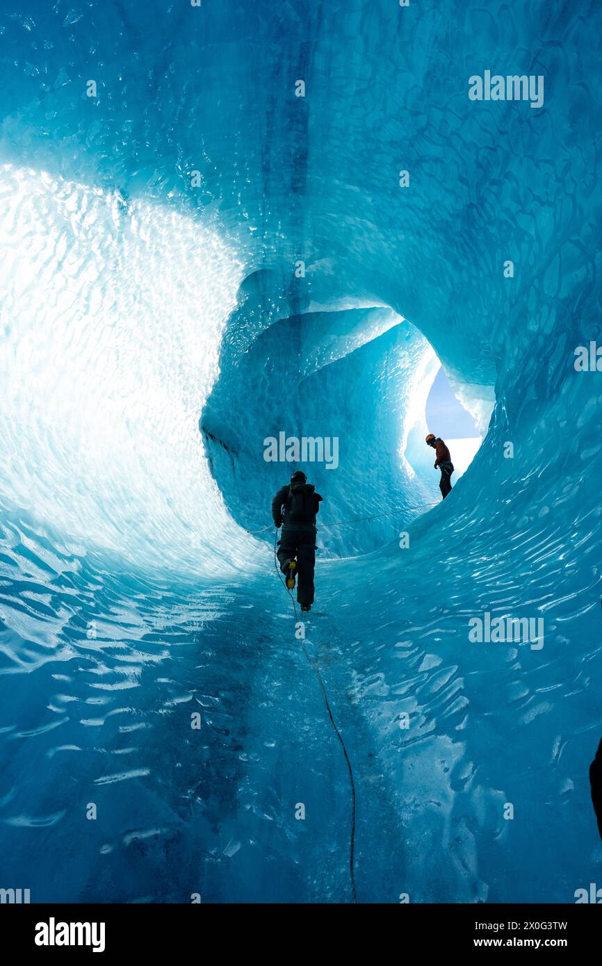 Man Climbing Up Glacier Cave in Islanda - Winter Gear - Blue Iceberg Foto Stock