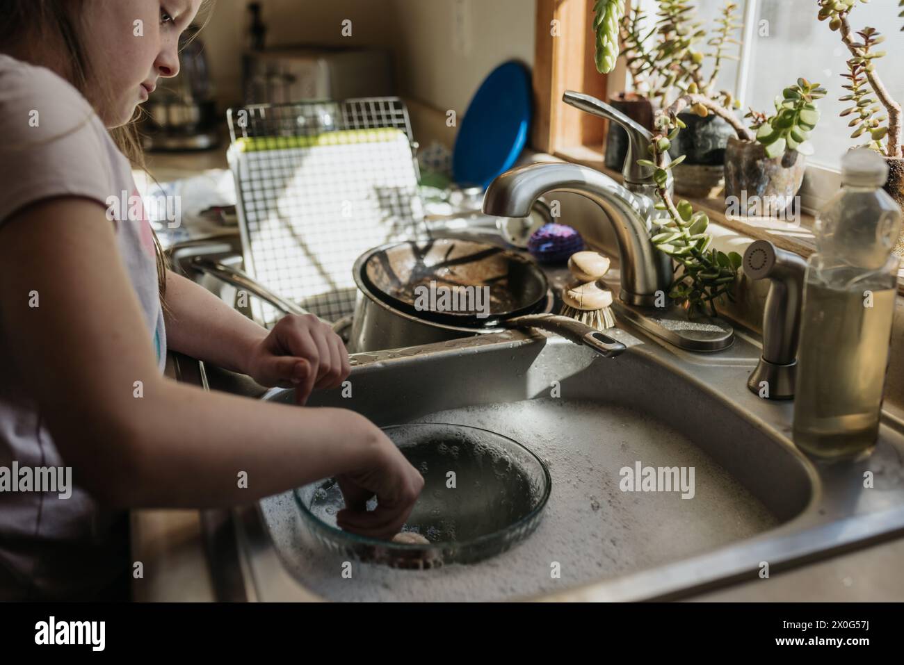 La ragazza lava il lavandino pieno di piatti sporchi in cucina a casa sua Foto Stock