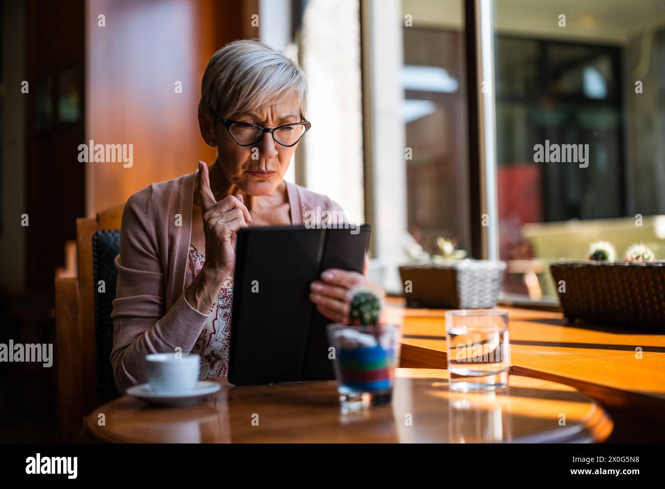 Una donna matura è seduta in una caffetteria e utilizza un tablet digitale. Foto Stock