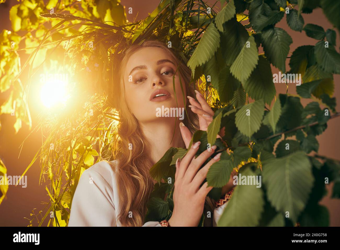 Una giovane donna con un abbigliamento tradizionale si erge graziosamente accanto a un albero adornato con foglie lussureggianti, incarnando un fascino fiabesco. Foto Stock