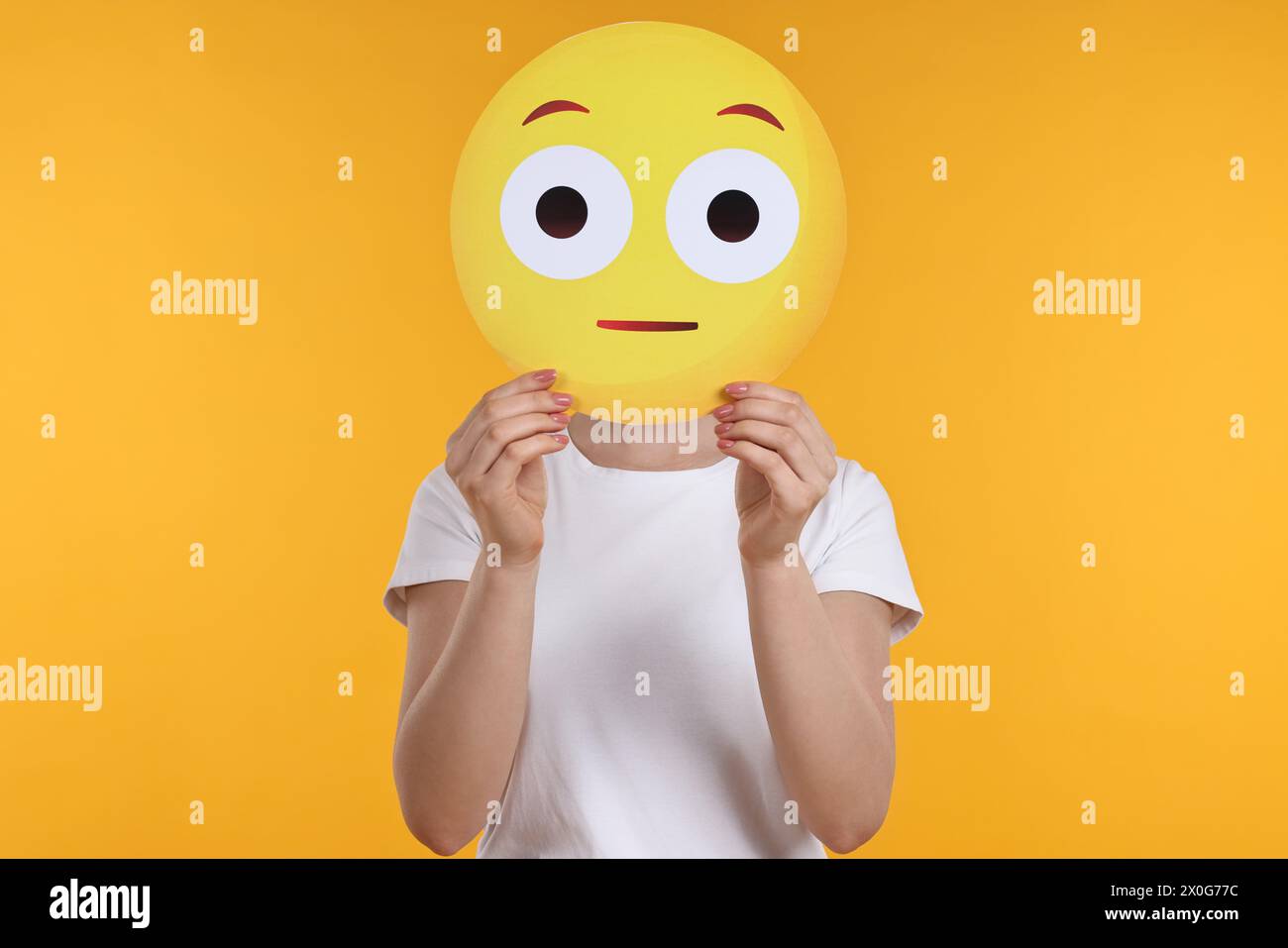 Donna che copre il viso con emoticon sorpresa su sfondo giallo Foto Stock