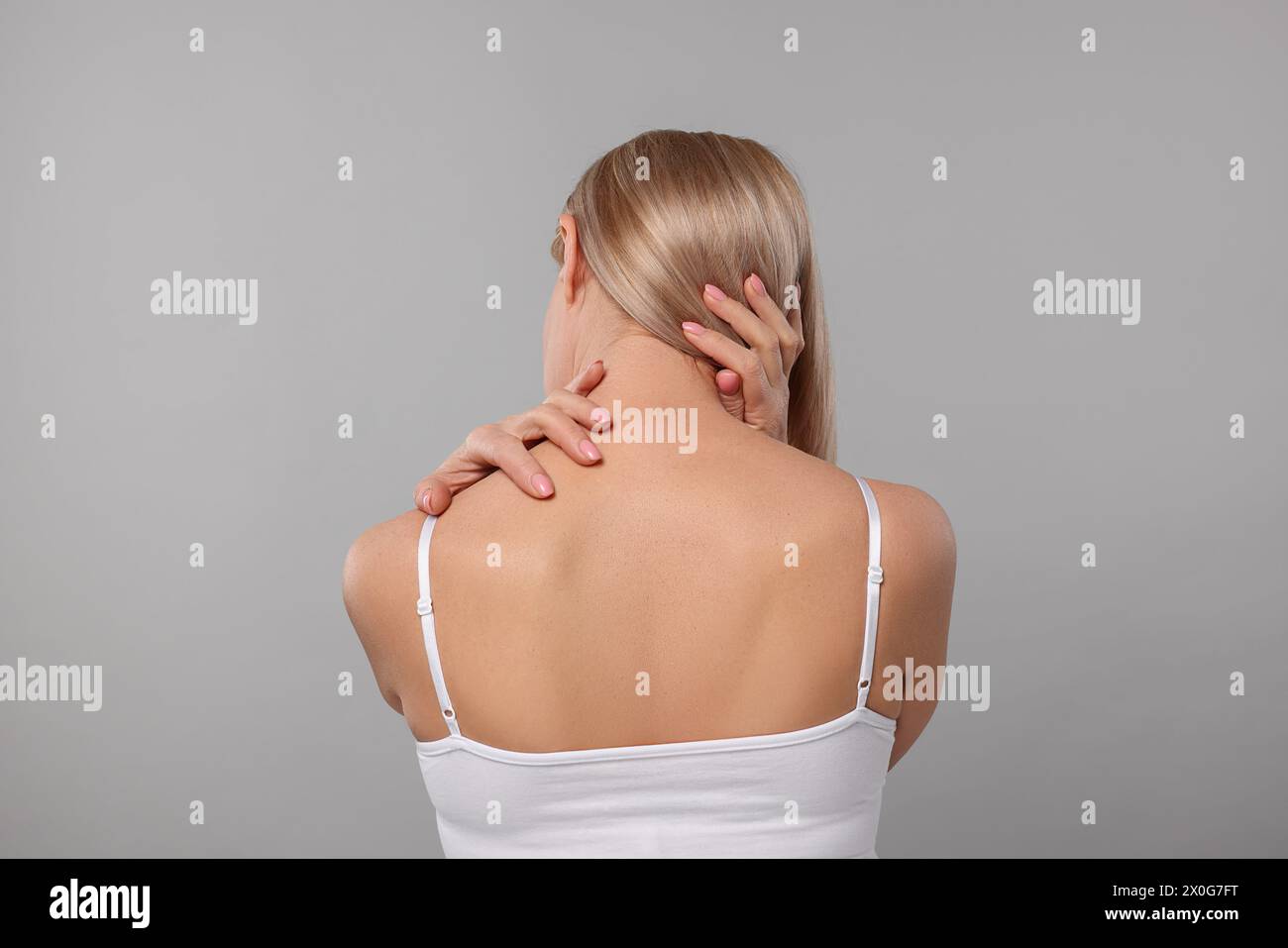 Donna che soffre di dolore al collo su sfondo grigio, vista posteriore Foto Stock