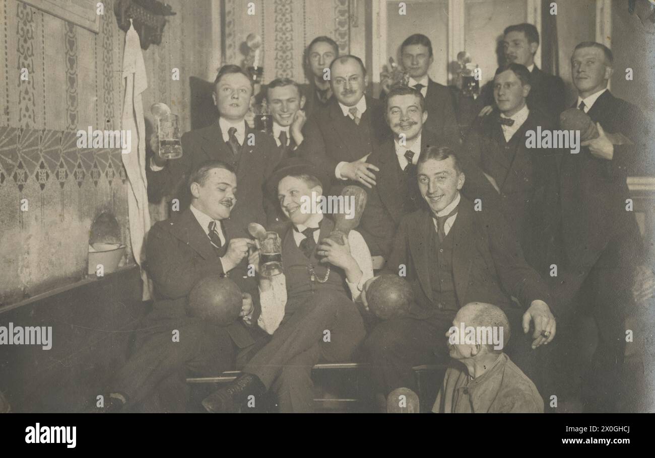 "Il gruppo del club di bowling si siede insieme per la foto di gruppo. Indossano abiti e tengono le palle in mano. Molti di loro bevono birra. In primo piano c'è un uomo vecchio e scarsamente vestito, il "ragazzo del bowling", che deve mettere le biglie da bowling. [traduzione automatizzata]' Foto Stock