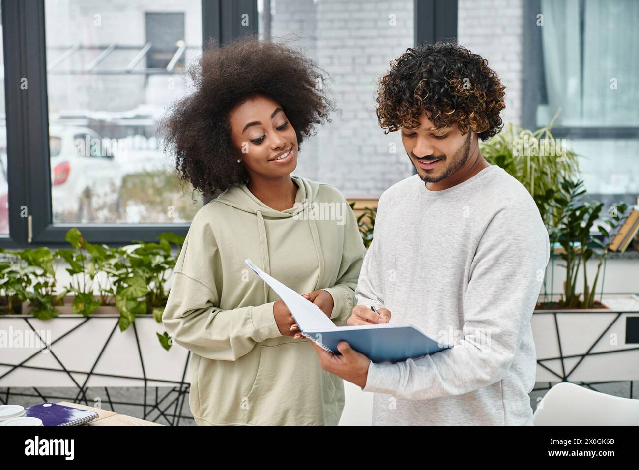 Un uomo e una donna di culture diverse si concentrano intensamente su un pezzo di carta, impegnati in un'esperienza di apprendimento condivisa. Foto Stock