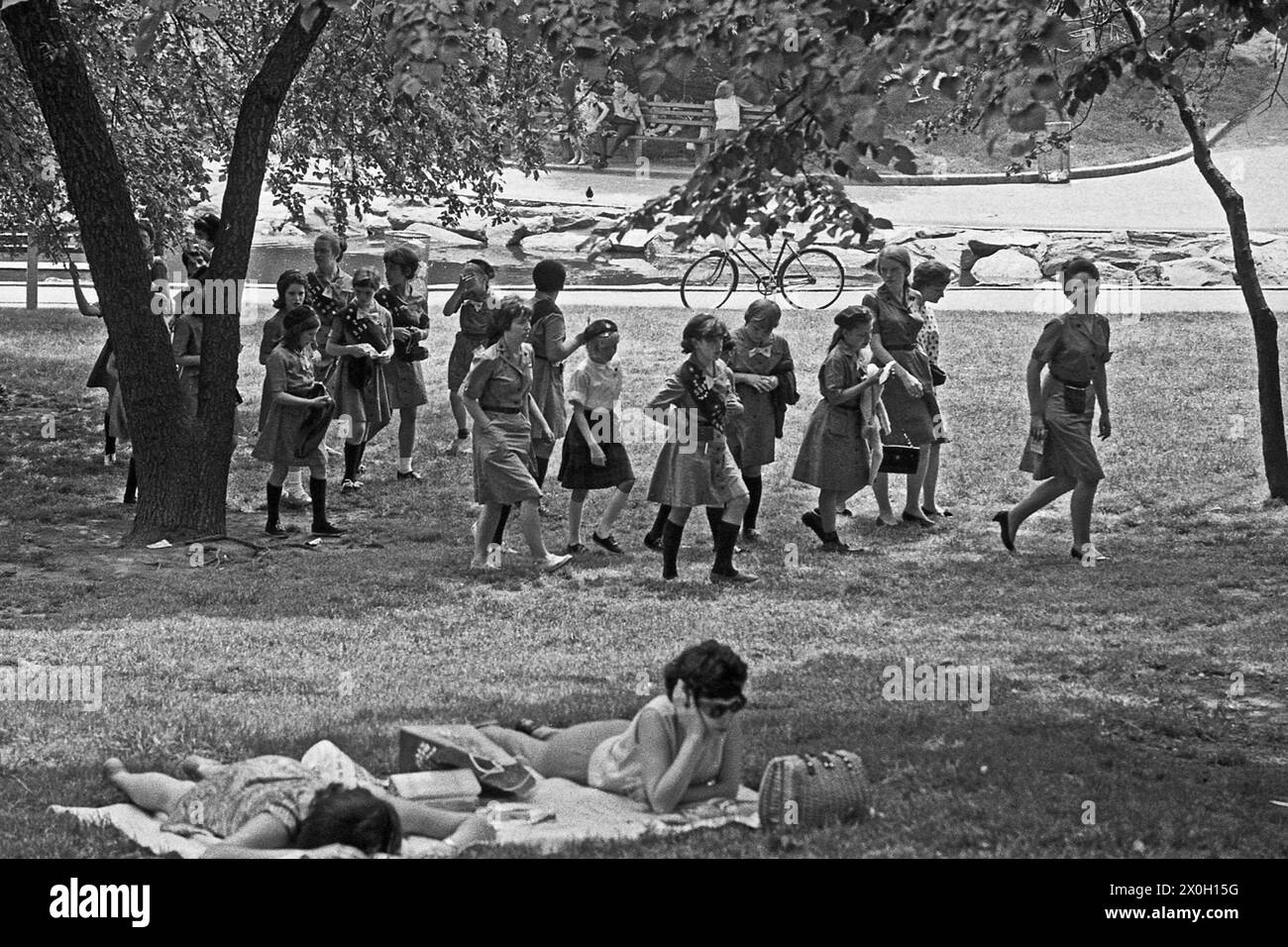 Un gruppo di scout femminili in uniforme passeggiate passato due donne giacente in un prato di Central Park. Foto Stock