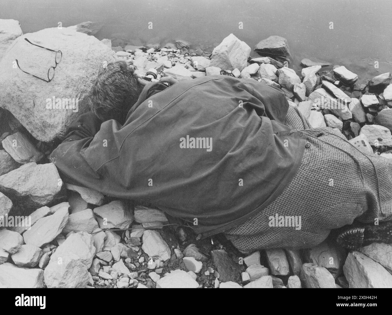 Un uomo si trova sulla riva di un lago o di un fiume e fotografa la superficie dell'acqua (colpo non datato). [traduzione automatica] Foto Stock