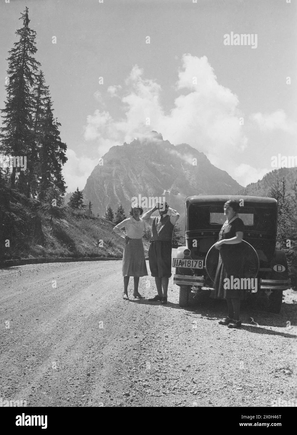 Due donne e un uomo si trovano accanto ad un Hupmobile Serie e su una strada nelle Dolomiti italiane. [traduzione automatica] Foto Stock