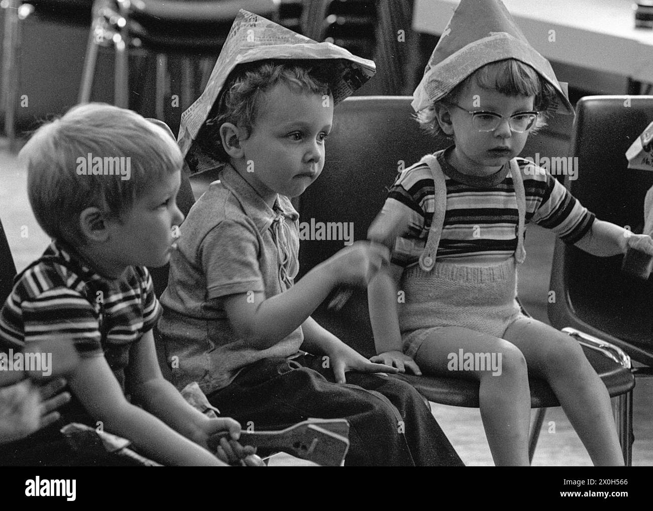 Con cappelli di carta fatti in casa e un sonaglino nelle loro mani, i bambini fanno musica [traduzione automatica] Foto Stock