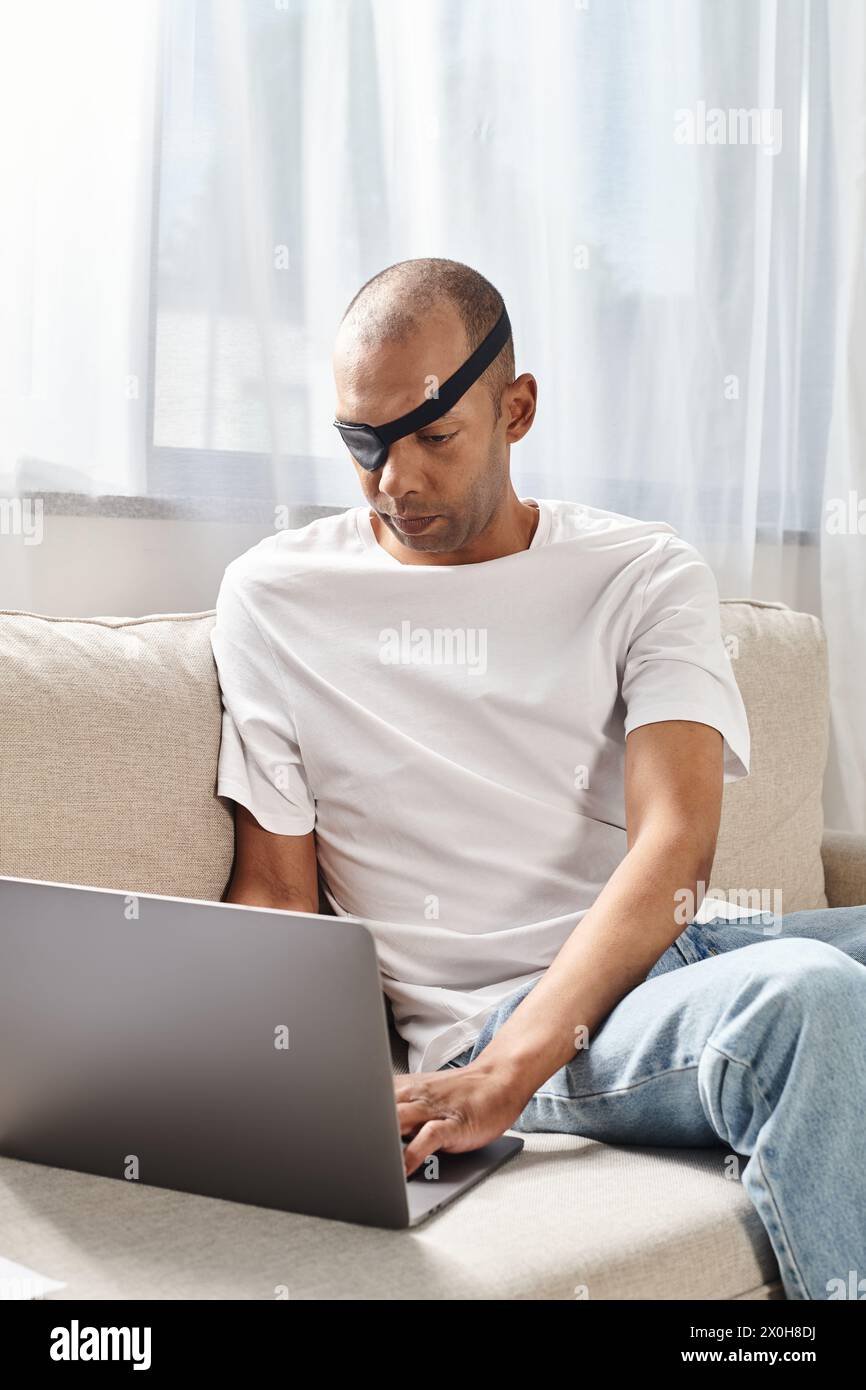 Uomo afroamericano con sindrome da miastenia gravis che usa un computer portatile su un divano. Foto Stock