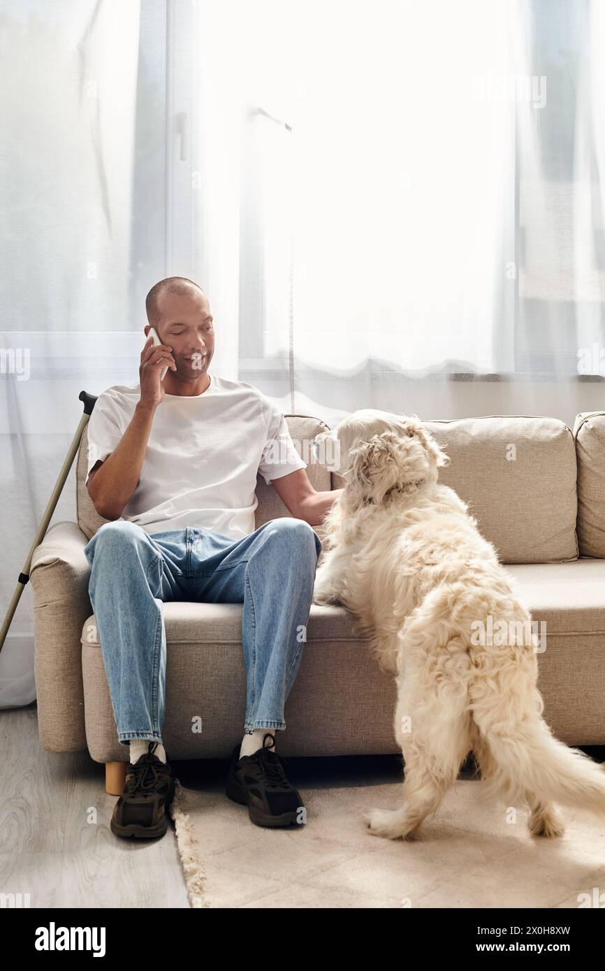 Un uomo con miastenia gravis parla al cellulare vicino al suo cane Labrador a casa. Foto Stock