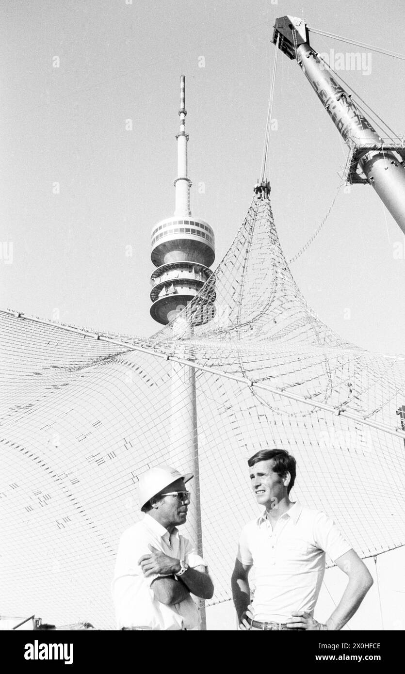 Due uomini stanno di fronte alla rete parzialmente rialzata del tetto della tenda per lo Stadio Olimpico. Sullo sfondo la Torre Olimpica [traduzione automatica] Foto Stock