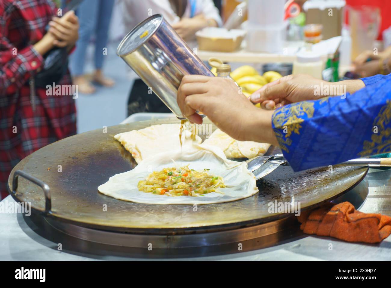 Immergiti nelle vivaci strade della Thailandia con questa vivace scena. Un venditore esperto prepara sapientemente roti croccanti, un amato cibo di strada Foto Stock