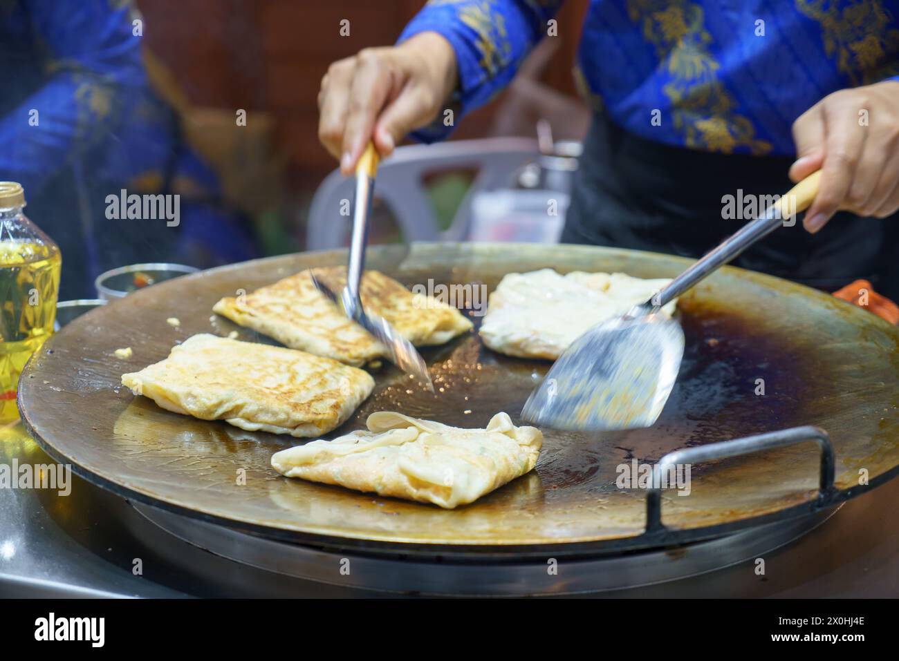 Immergiti nelle vivaci strade della Thailandia con questa vivace scena. Un venditore esperto prepara sapientemente roti croccanti, un amato cibo di strada Foto Stock