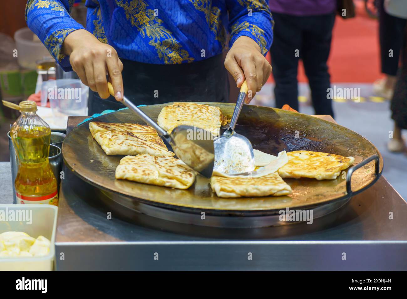 Immergiti nelle vivaci strade della Thailandia con questa vivace scena. Un venditore esperto prepara sapientemente roti croccanti, un amato cibo di strada Foto Stock
