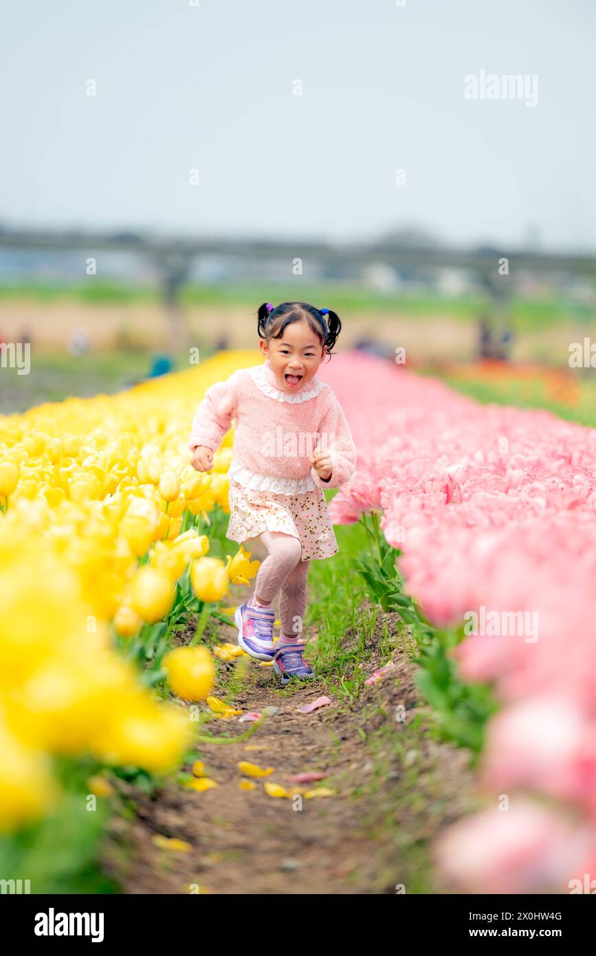Una bambina corre nel bel mezzo di un giardino fiorito di tulipani. Foto Stock
