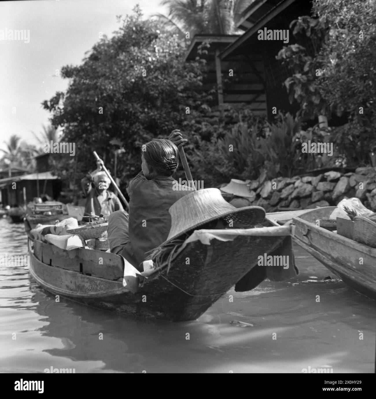 Una donna guida la sua barca di legno sul fiume Chao Phraya a Bangkok, Thailandia. Anche un vecchio viaggia verso di lei in barca. [traduzione automatica] Foto Stock