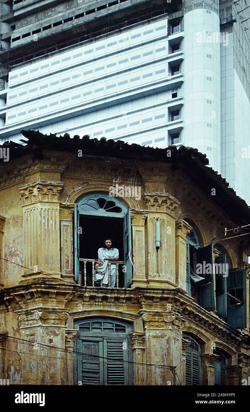 Vista di una vecchia casa d'angolo a Singapore. La facciata è scappare e scolorita. Il tetto è parzialmente rotto. Nella finestra superiore c'è una persona. Sullo sfondo un moderno ed alto edificio. [traduzione automatica] Foto Stock